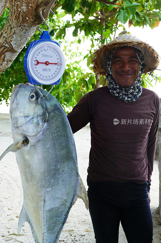 2016年7月27日，印度尼西亚，马拉图亚岛:一名印尼渔民骄傲地站在他的捕获物旁边——一个重达13公斤的Trevally Giant。